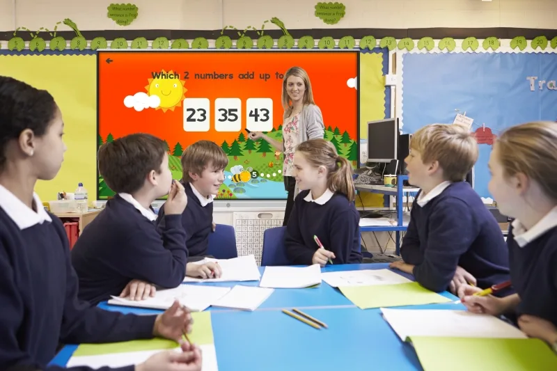 Pupils Sitting At Table As Teacher Stands By Whiteboard
